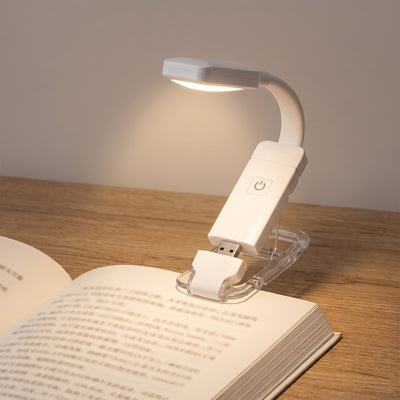 Book light clipped to open paperback glowing warm