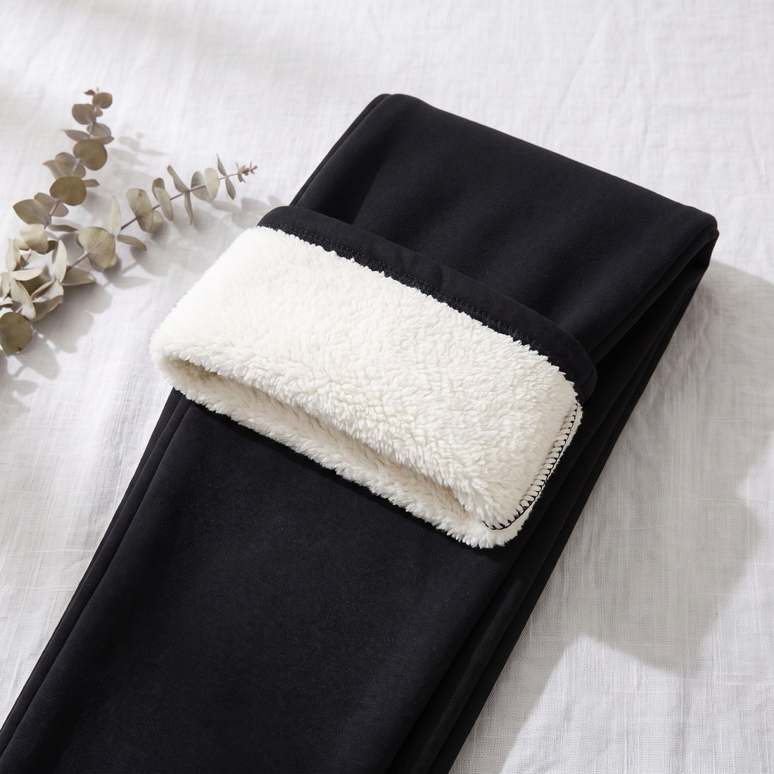 Black thermal leggings laid flat with the waistband folded to show the white fleece lining